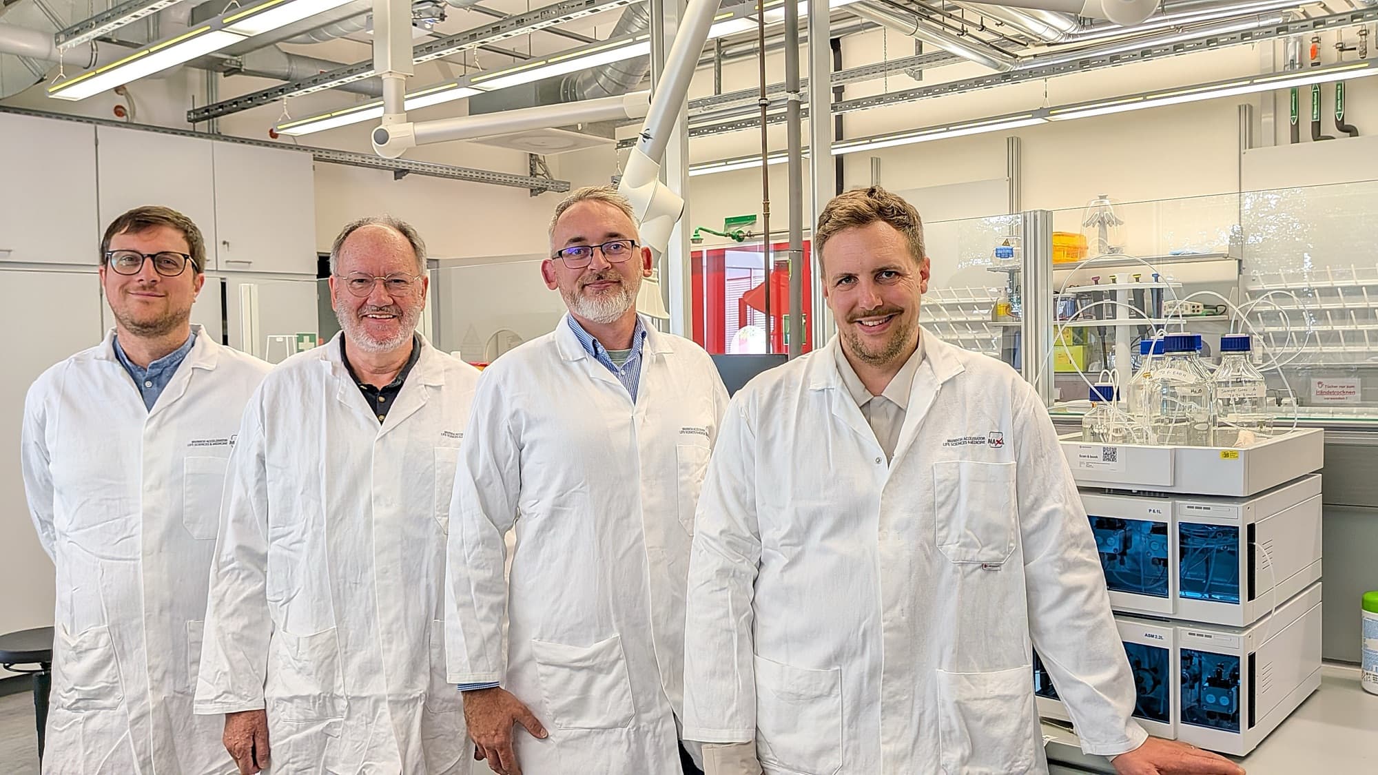 Stefan Munker, Ekkehard Leberer, Grzegorz Popowicz and Niklas Laasch in lab coats in the laboratory at BioM